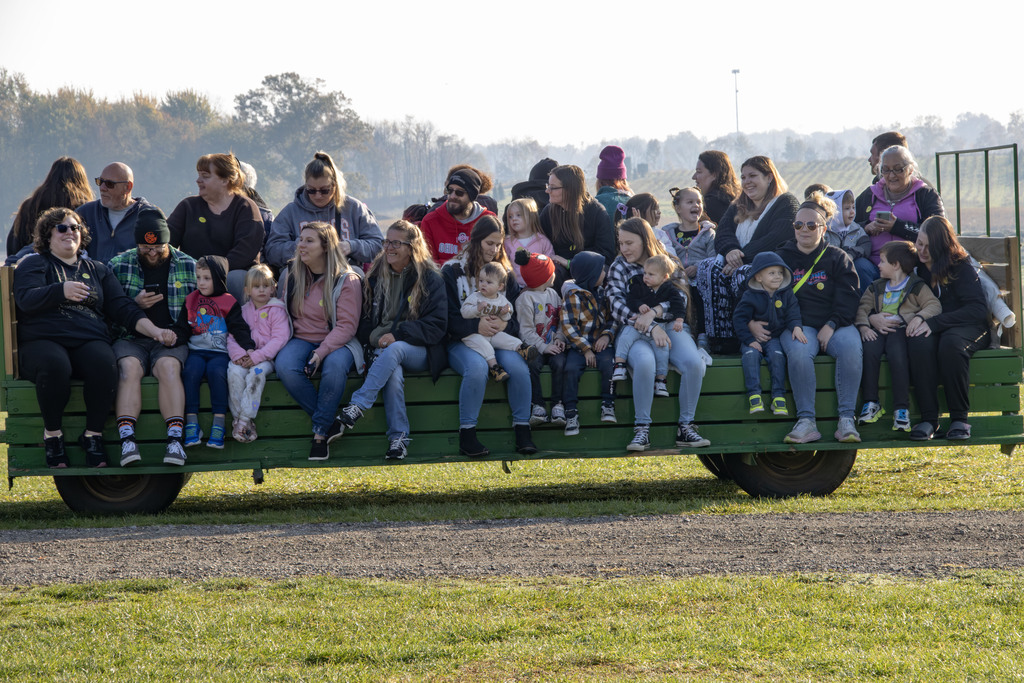 Several families sit on a trailer covered in hay bails