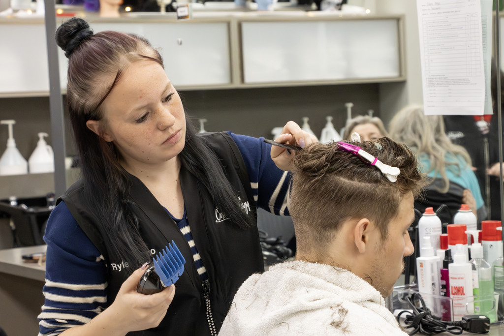 A student carefully cuts another students hair