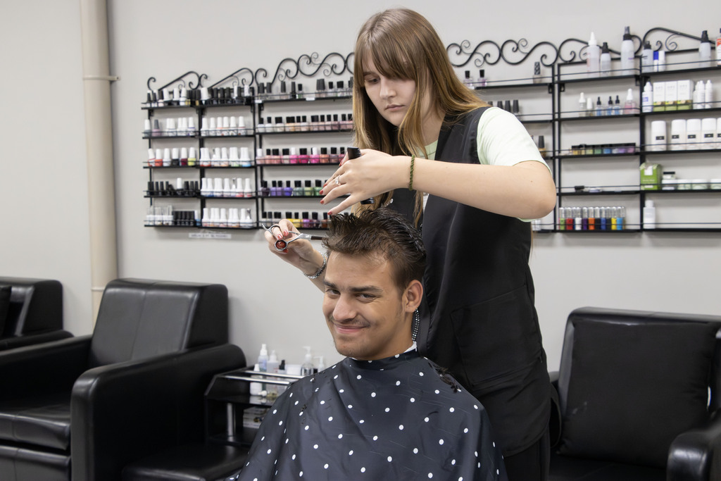 A cosmetology student cuts another students hair