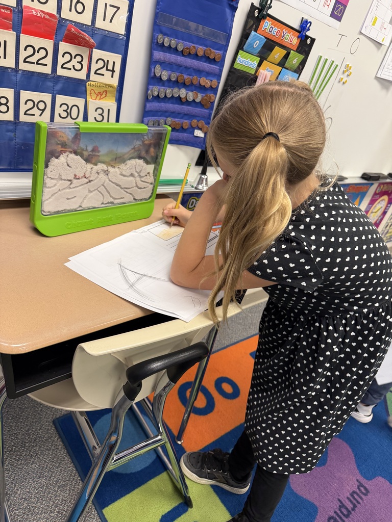 A students looks at the ant farm while writing on a piece of paper