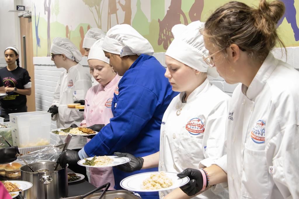 6 people wearing chef's jackets plate food