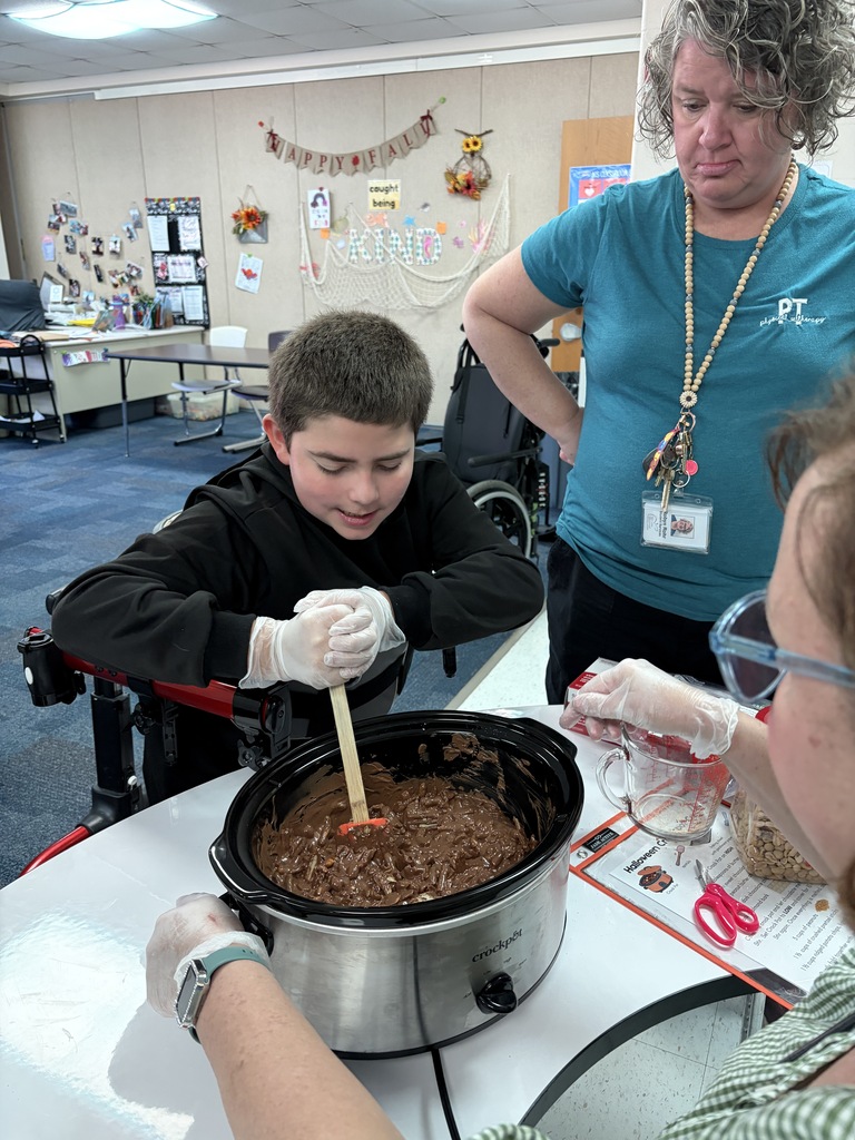 A student stirs the candy in a crockpot while two staff members watch