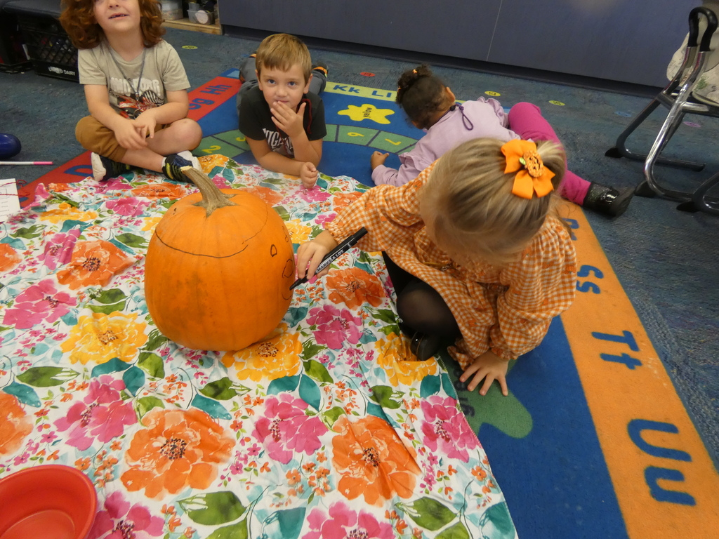 a student draws a face on the pumpkin while others watch