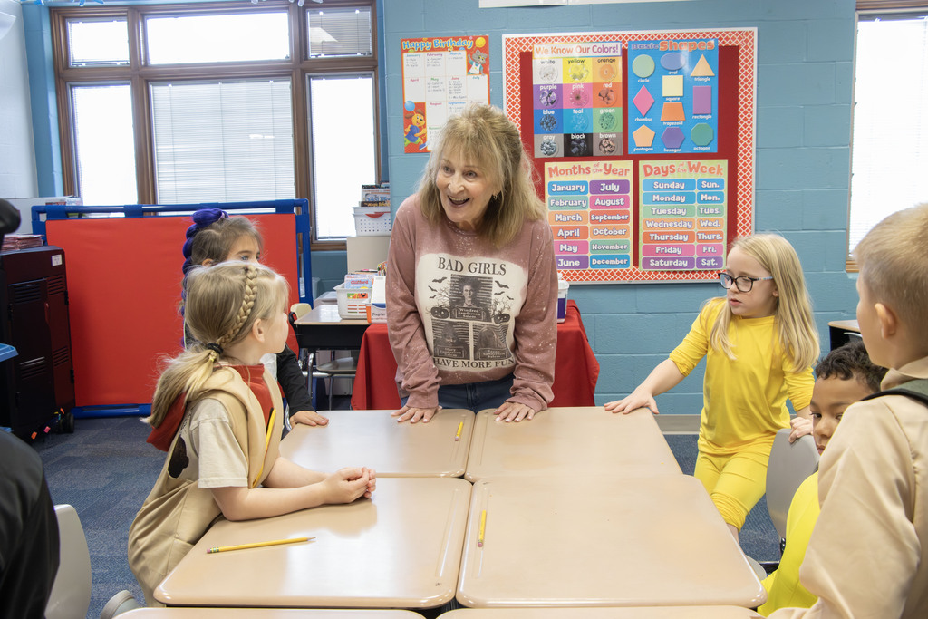 An adult smiles at students dressed in costume