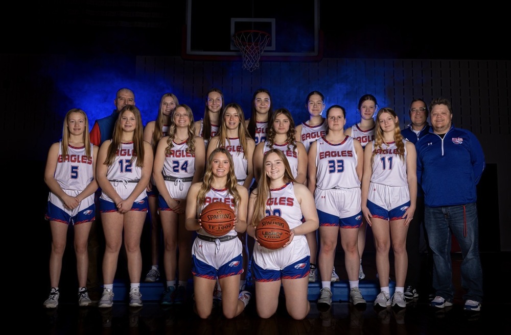 14 Eagles girls basketball players smiling at the camera with 3 coaches standing next to them.
