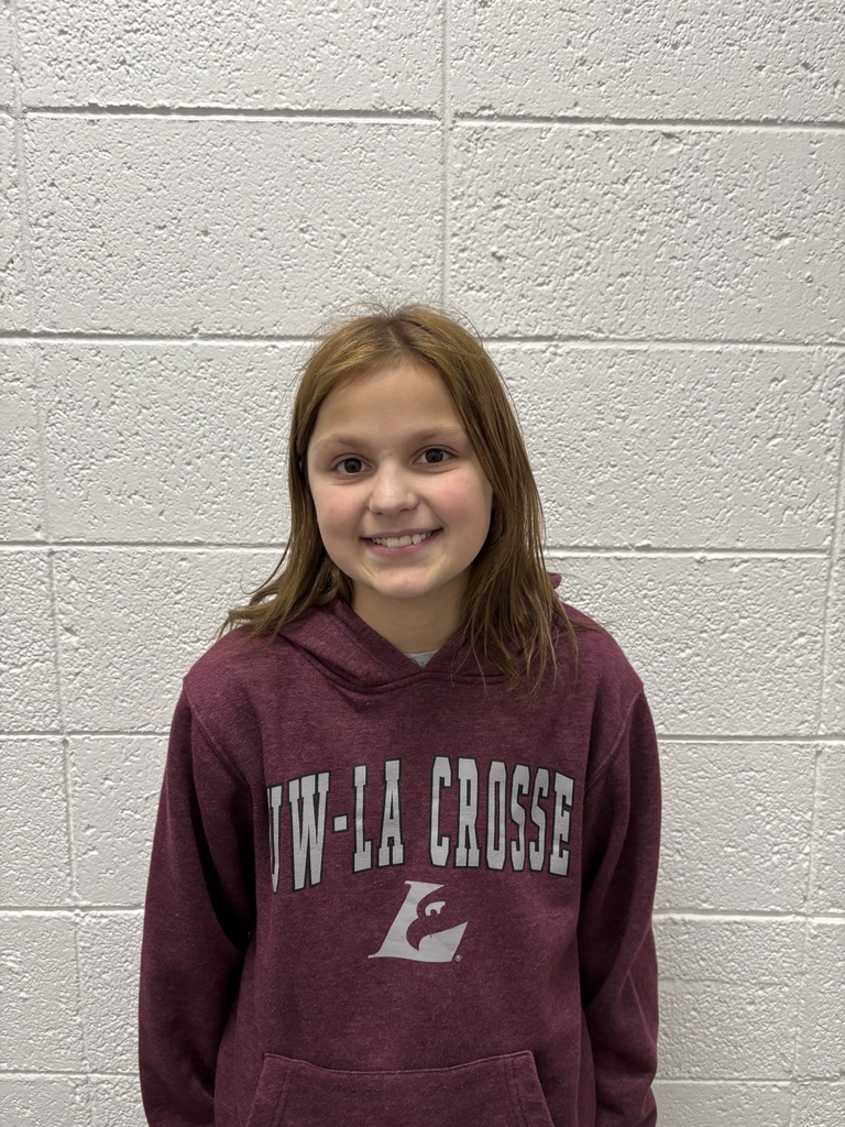 A smiling young child with light brown hair stands against a white cinderblock wall, wearing a maroon UW–La Crosse hoodie.