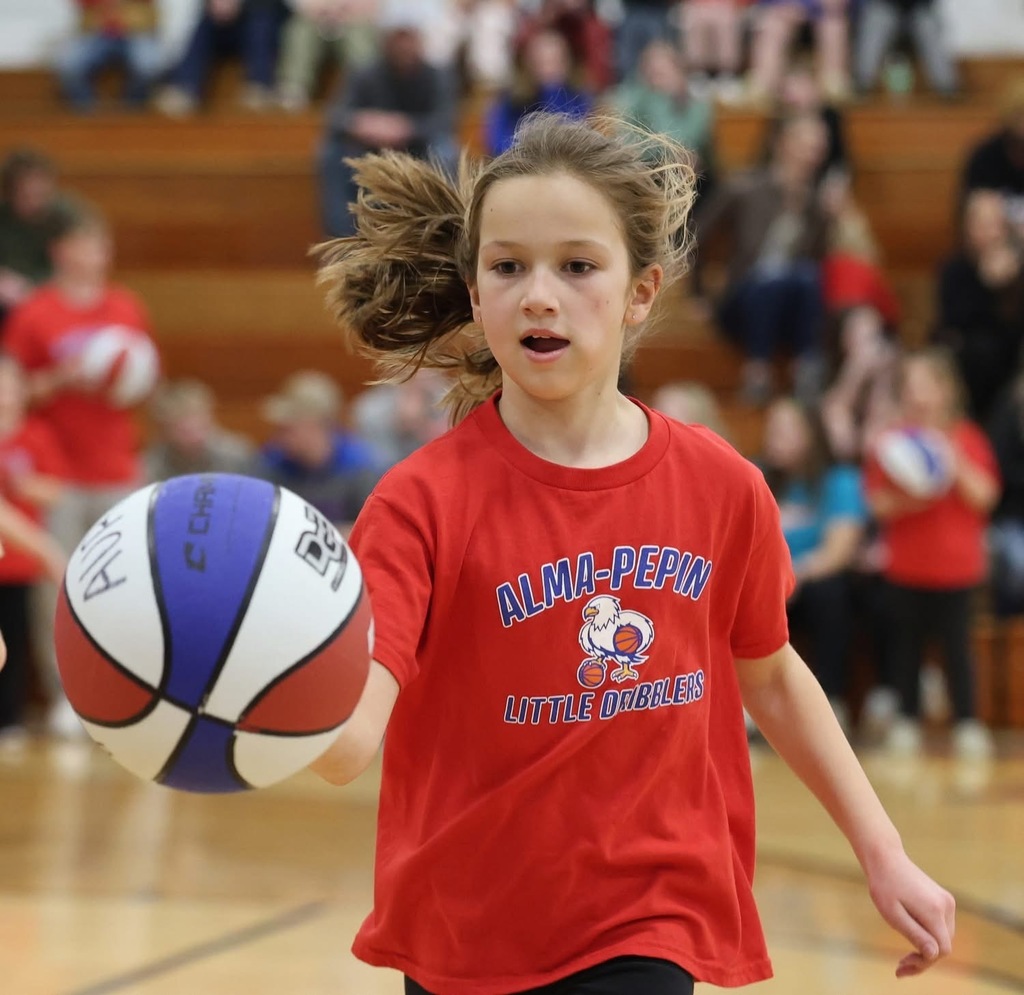 A young girl is captured mid-stride while dribbling. Her hair is flying behind her, showing her speed and movement.
