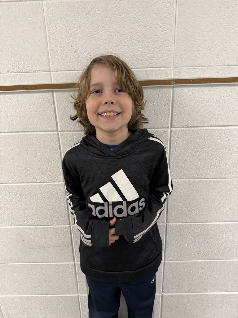 Smiling student standing against a white brick wall.