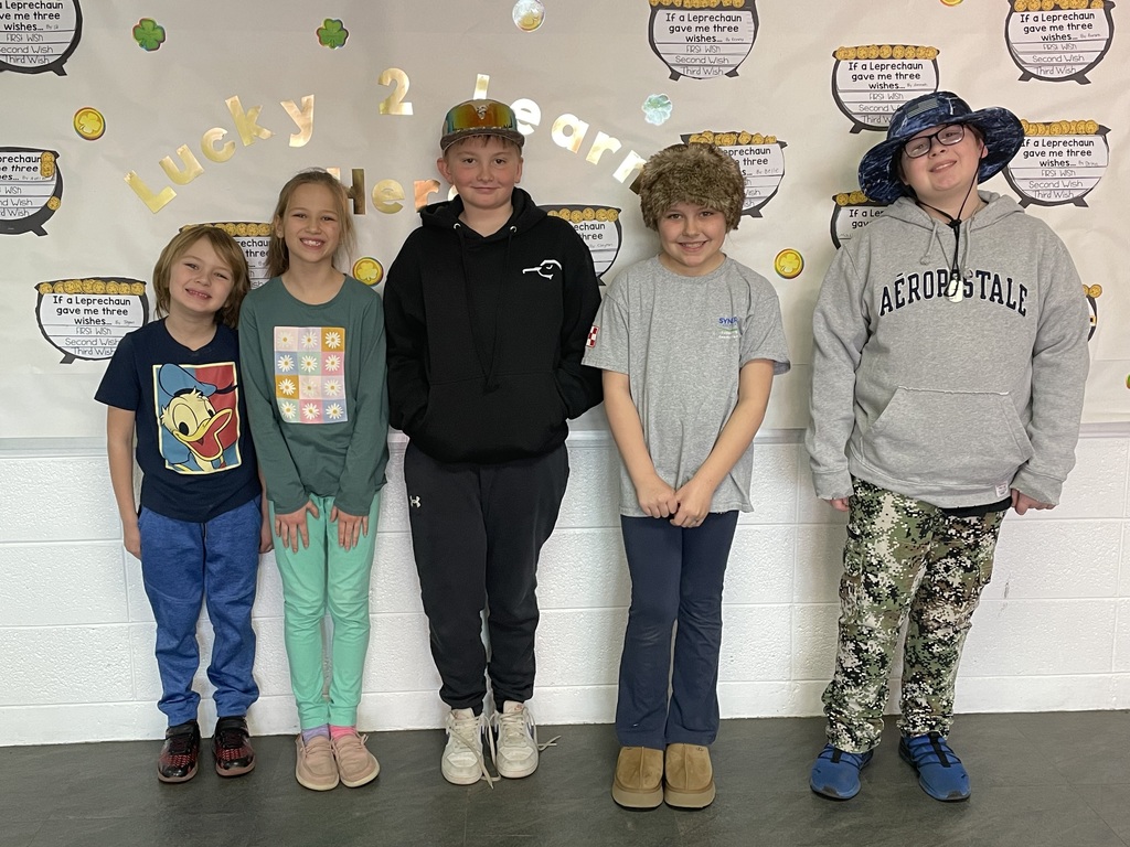  Gemini said In the image, five children are standing in a row in front of a white wall decorated with a "Lucky 2 Learn" banner and St. Patrick's Day-themed "If a Leprechaun gave me three wishes..." worksheets.