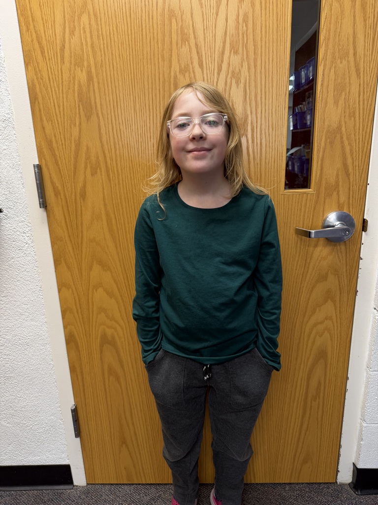 Second grader, Madison Brownell standing in front of a door and smiling.