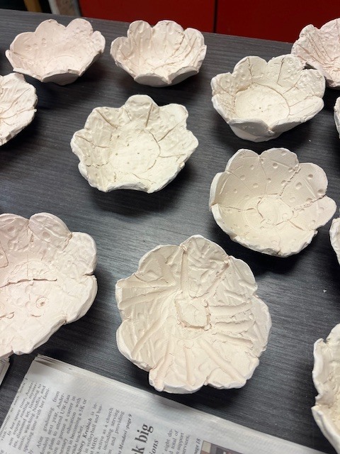 A collection of small, handmade white clay bowls shaped like flowers. Each bowl has petal-like edges and textured lines etched into the center to mimic a floral pattern.