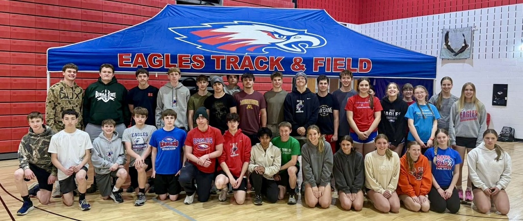 Track athletes standing and kneeling infront of their new tent.