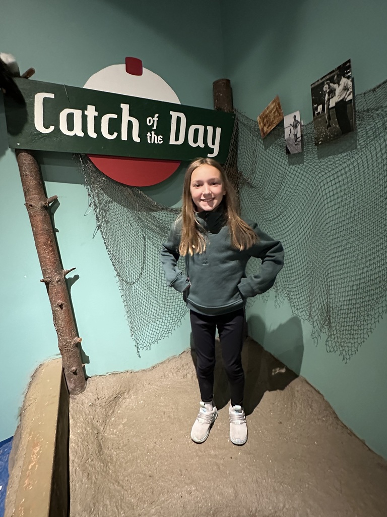 Quinn standing infront of a sign that says "Catch of the Day"