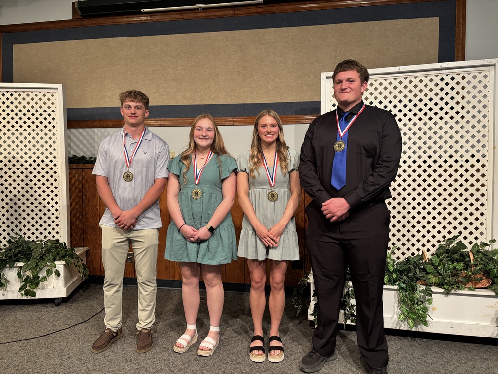 Four high school students stand side by side on a decorated stage, each wearing a medal and posing for a photo after an awards ceremony.