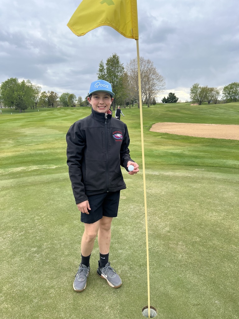 Middle school golfer holding a gold ball and standing by the flag and hole.