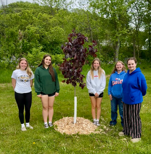 Students standing and smiling next to tree.