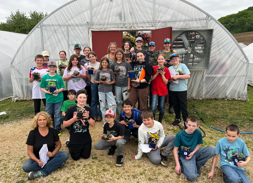 The sixth graders holding their plants infront of the greenhouse.