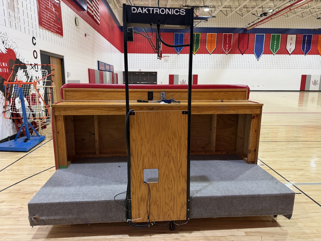 back side of score table that is on wheels with bar like seating spot, made of wood and gray carpet floor front is red and white with a riverman logo in the middle, the front is a heavy plastic material
