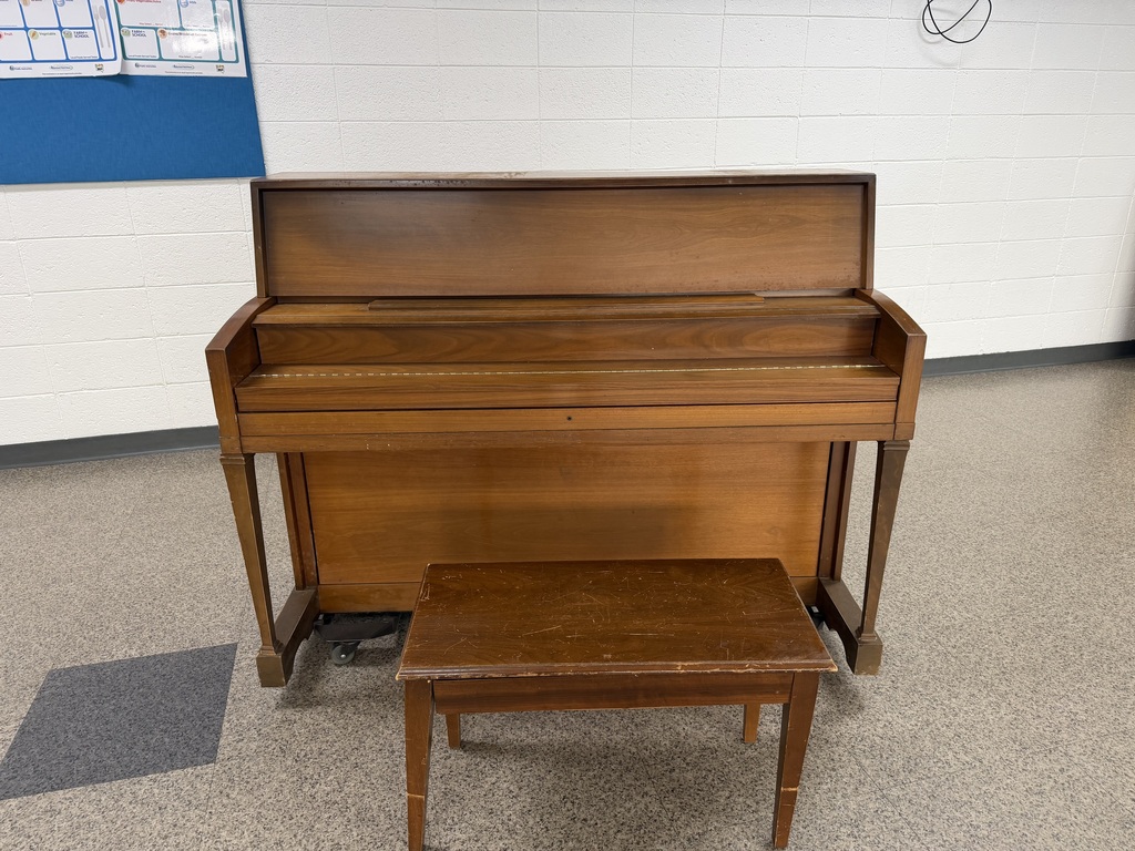 Wood piano with the cover on the keys down and the bench seat down so you can sit on it. Normal size.