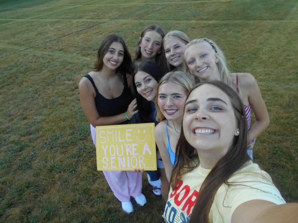 Girls smiling and holding a sign that says, "Smile You're A Senior" .
