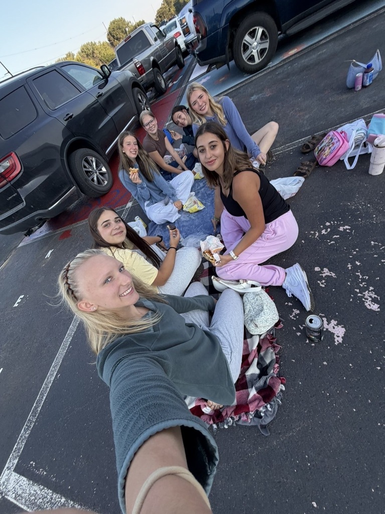 Girls sitting in a parking lot on blankets and eating breakfast.
