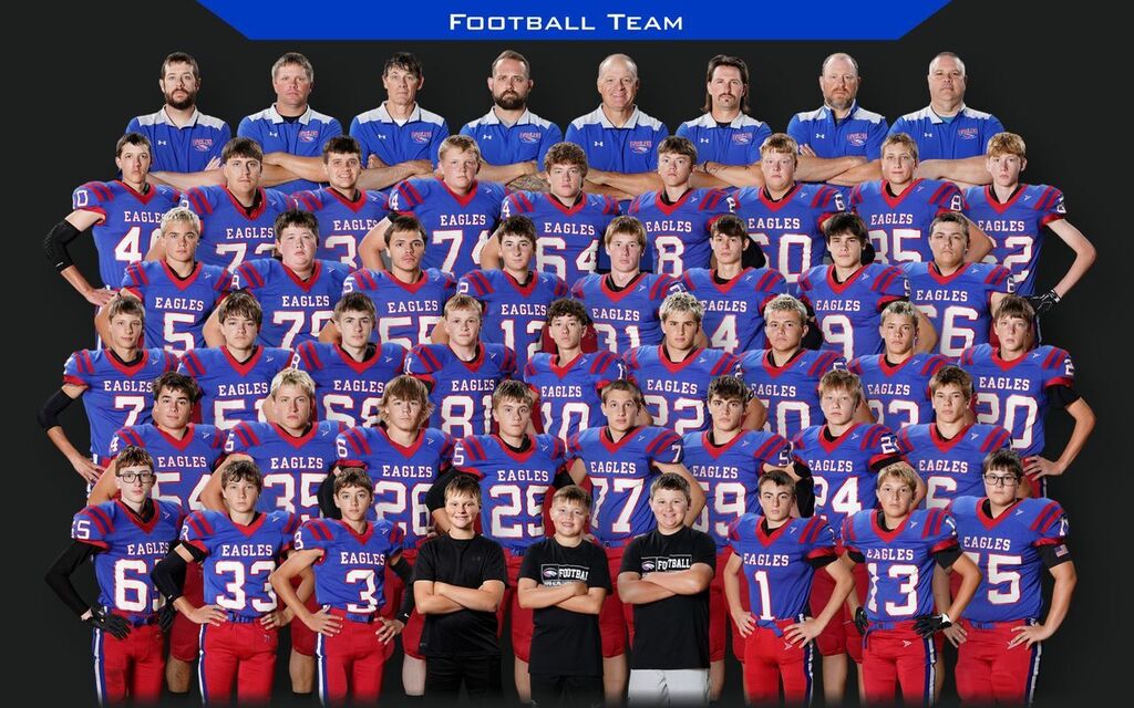 A large football team poses for a team photo, with coaches standing in the back and players in blue and red Eagles uniforms arranged in several rows. Three younger children wearing black football shirts stand in front.