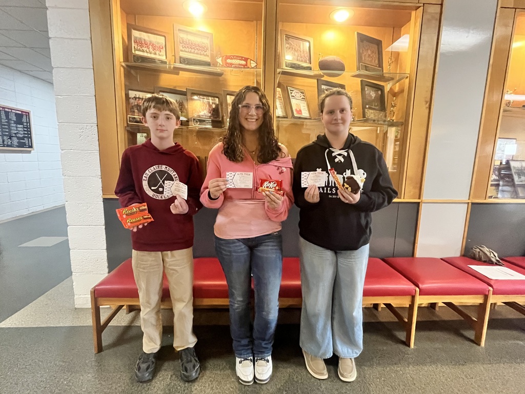 Three students stand in front of a school display case, each holding a small white raffle ticket and a candy bar.