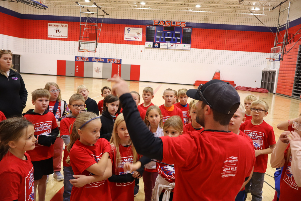 A teacher explaining to a large group of students in a gym.