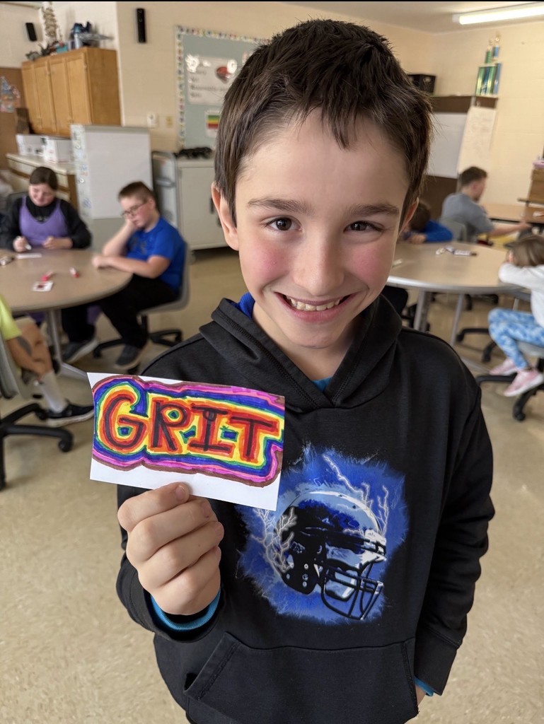 Student holds colorful paper that says "grit"