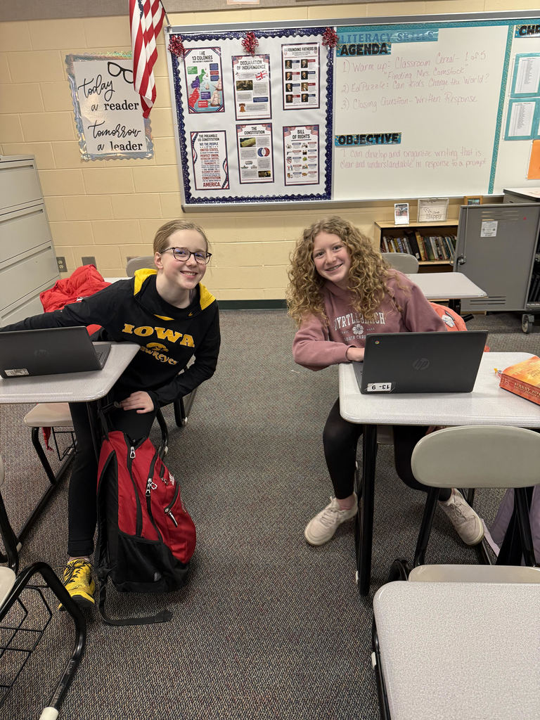 2 smiling students work on newspaper project in classroom