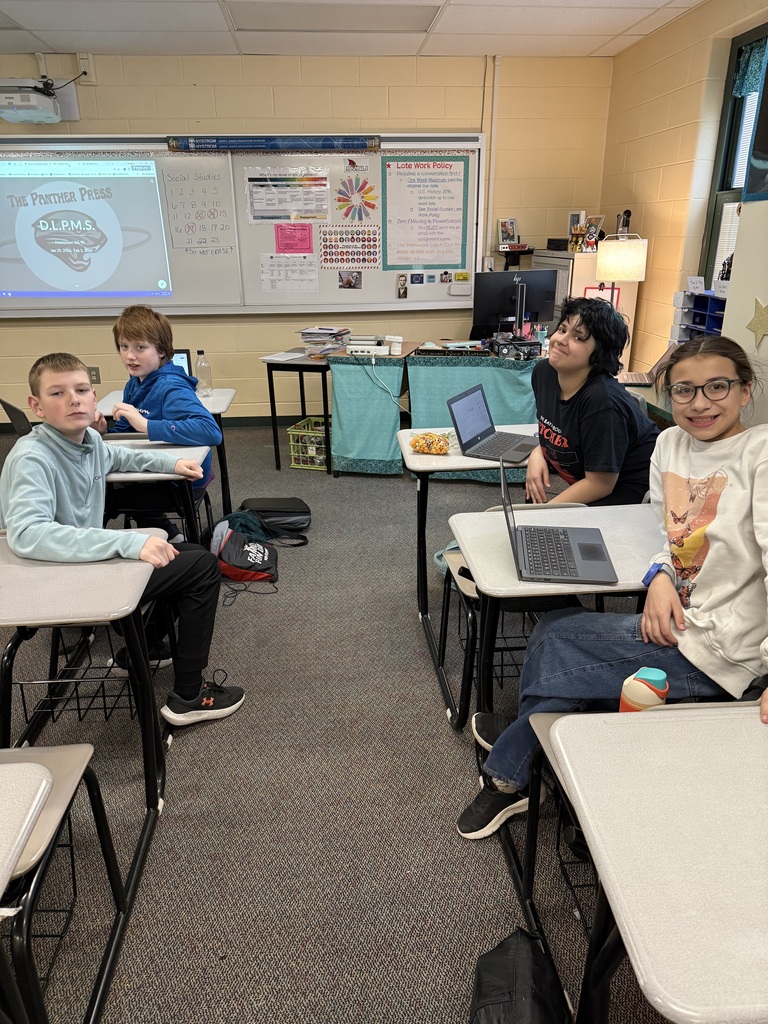 4 middle school students sit at their desks, working on the school newspaper