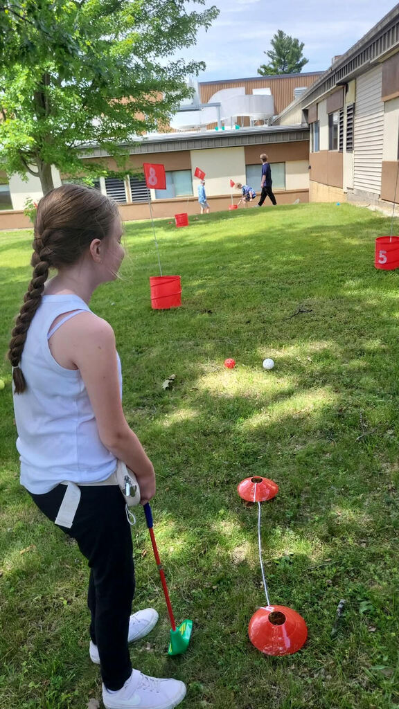 Ivey wears black leggings, a light blue tank top, white sneakers and a braid in her hair as she plays bucket golf in the grass