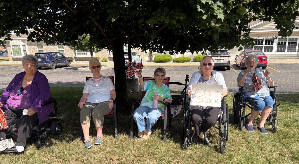 Arbor Grove residents (5) sit in chairs under tree to see students as they leave school on 1st day