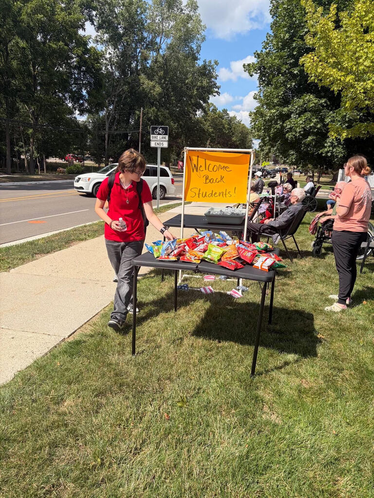 APS student takes snack from snack table provided by Arbor Grove (neon orange paper sign says "Welcome back students!")