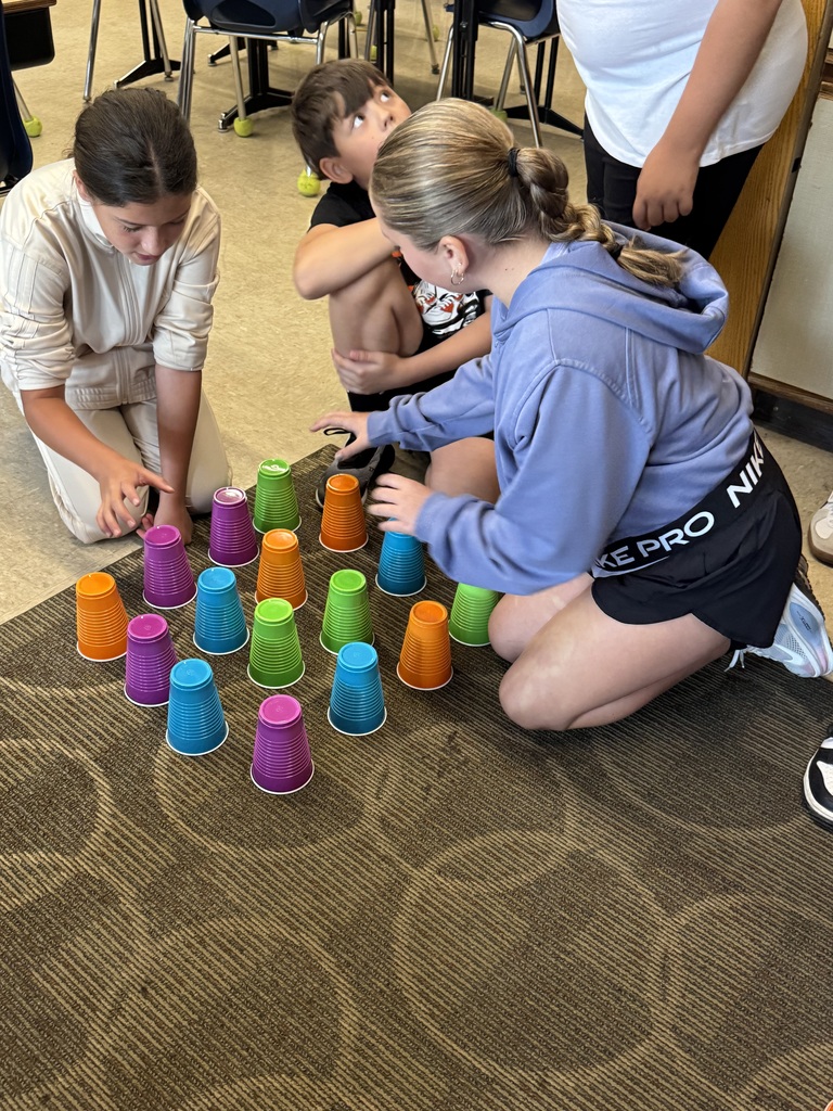 Three 5th graders using orange, teal, green, and purple cups to learn math in the classroom