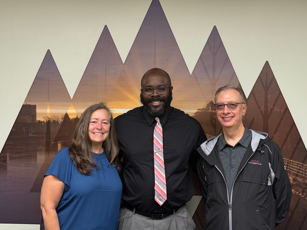 AMA Board of Education members Lisa Thayer, Lenny Avery, and Darrin Lightner standing together and smiling in front of a mural with a geometric mountain design and sunset background.