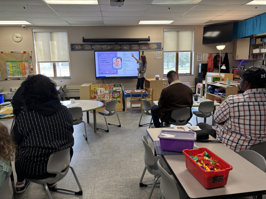 Dr. Jamie McClintic at the smart board presenting to a group of parents sitting in classroom chairs.