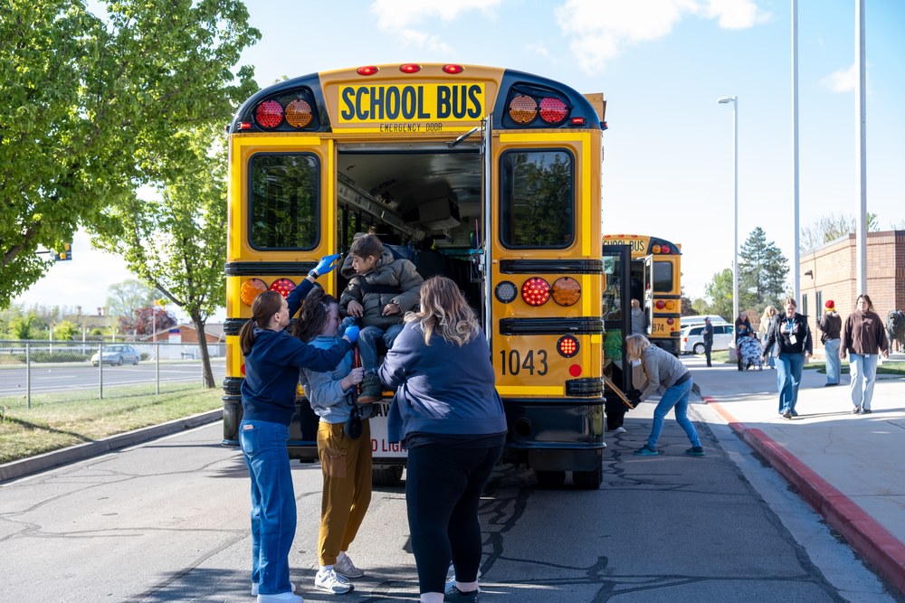 Student being lowered out of  the rear hatch of a schoolbus by staff members.