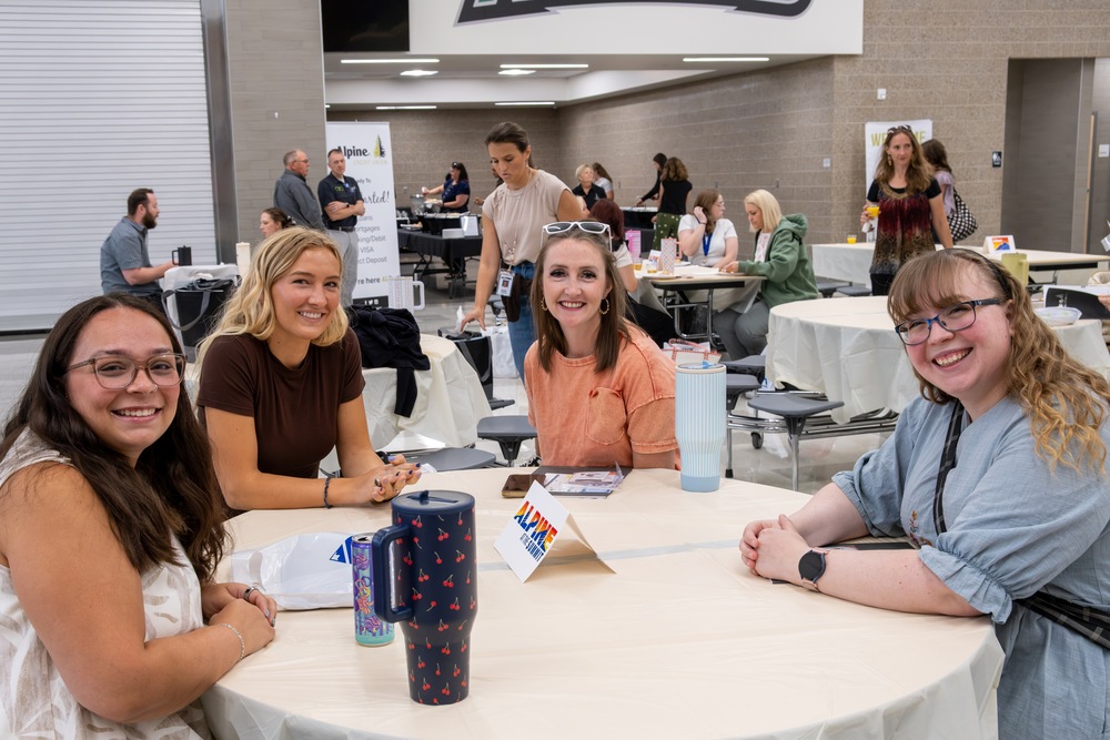 New teachers sitting around a lunch table smiling at the camera.