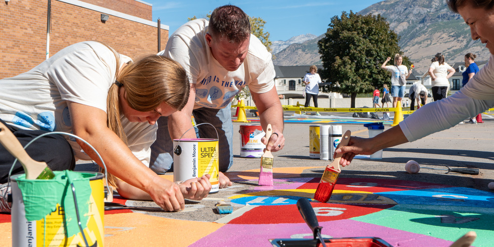 Volunteers painting recess games on blacktop behind school