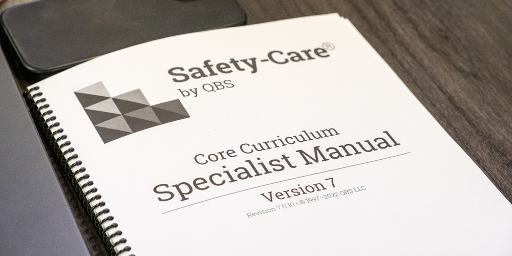 Safety-Care training booklet on a table. The booklet says Core Curriculum Specialist Manual Version 7 on the front.