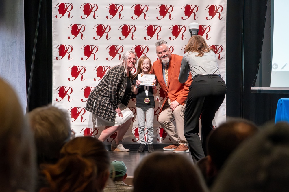 Student posing with superintendent and administrator holding an award.