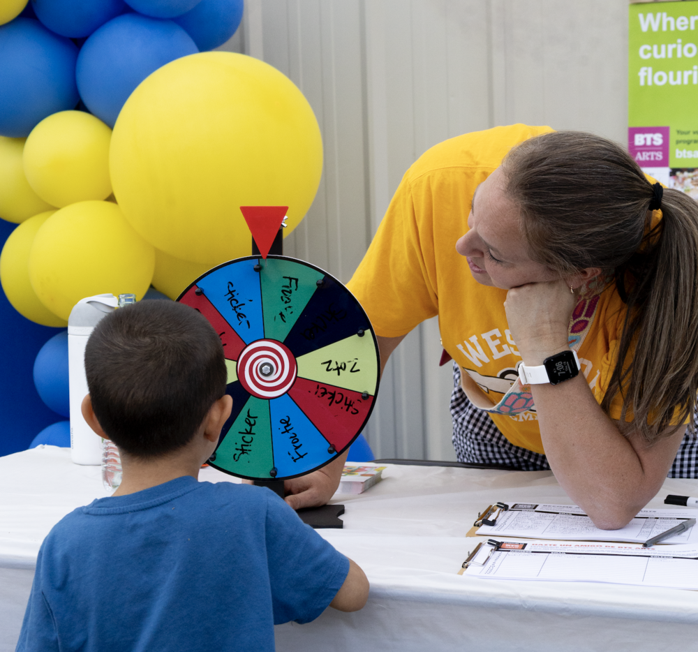 Little boy and teacher lookng at a carnival game with balloons in the background