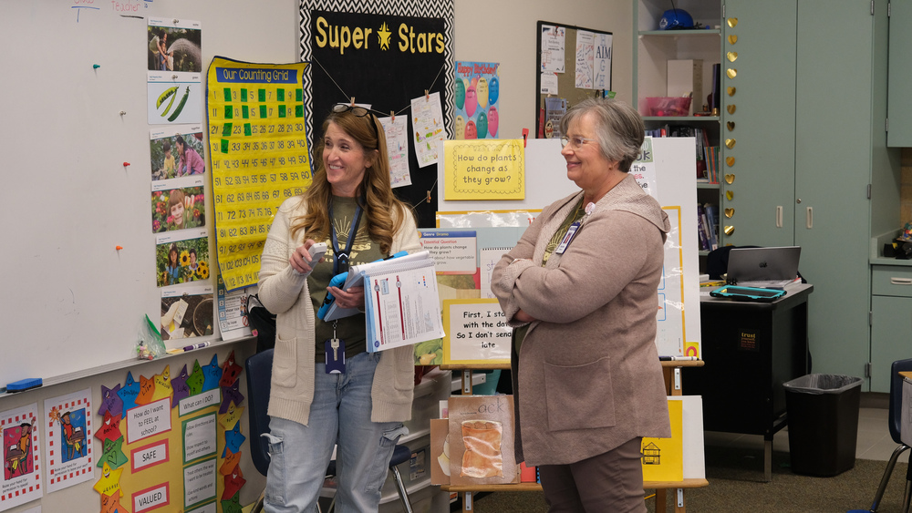 Two employees standing near eachother at the front of a classroom.