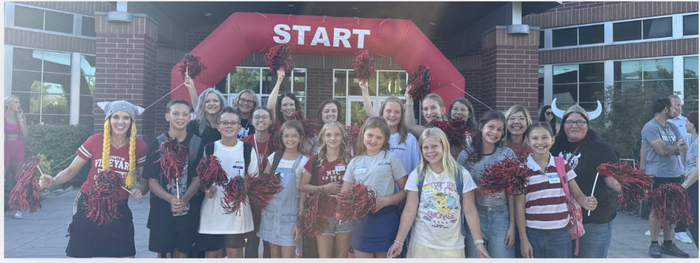 6th grade students and teachers standing and shaking black and red pom-poms in front of the brick school