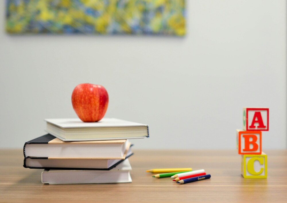 This is an image of stacked books, an apple, ABC blocks, and colored pencils to represent a "Back to School" mindset