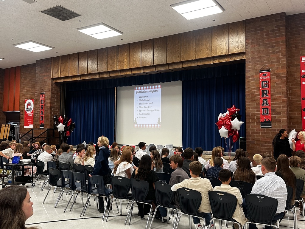 Students sitting in chairs in the lunchroom, facing the screen.