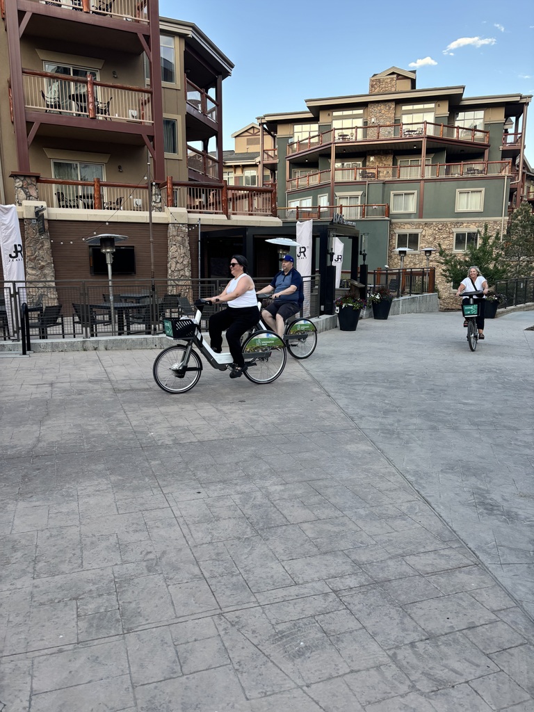 Three people riding bikes with building behind them. 
