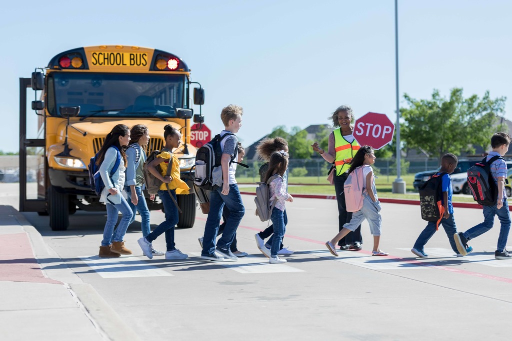 Crossing guard holding stop sign helping large group of students cross street