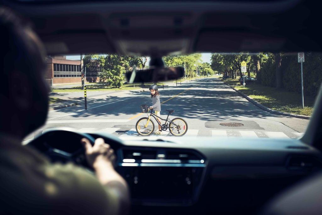 View of girl walking bicycle across street in crosswalk from inside vehicle